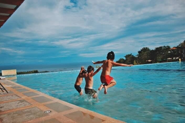 three kids jumping on the pool