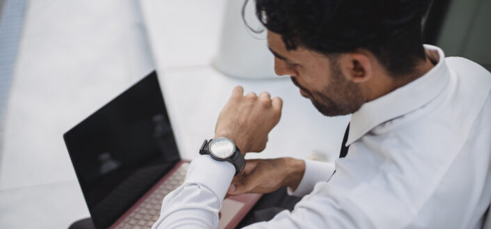corporate man checking watch while using laptop