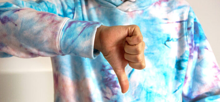 A person in tie dye sweater doing thumbs down