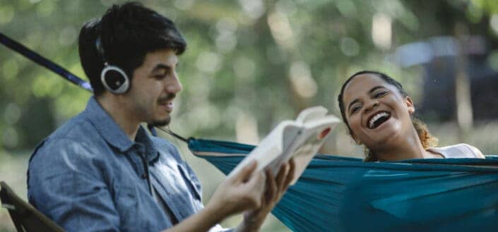 Happy multiethnic couple with book and hammock 