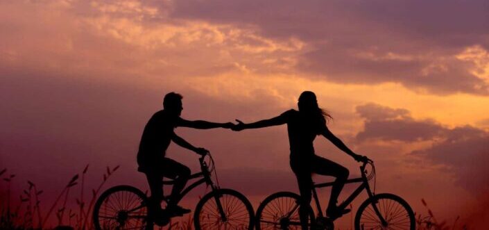 Silhouette of a couple holding hands while riding bikes
