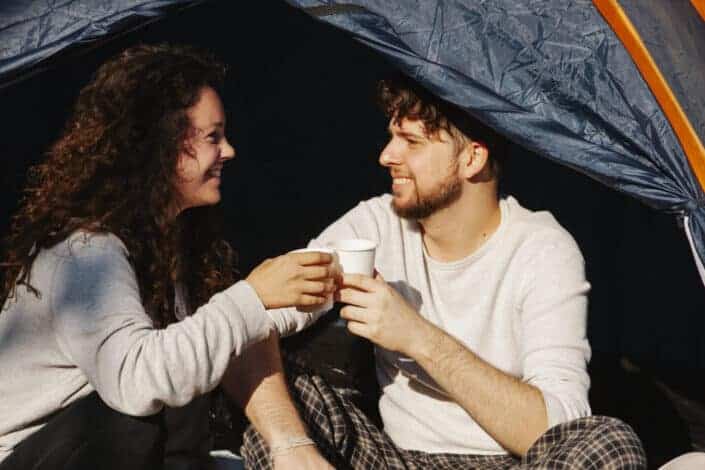 Couple inside the tent drinking coffee on a Styrofoam cup on an early sunny morning