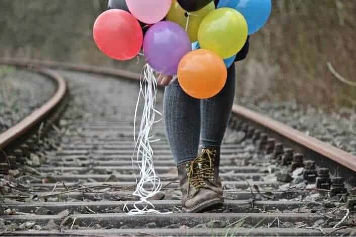 person walking on train track holding balloon