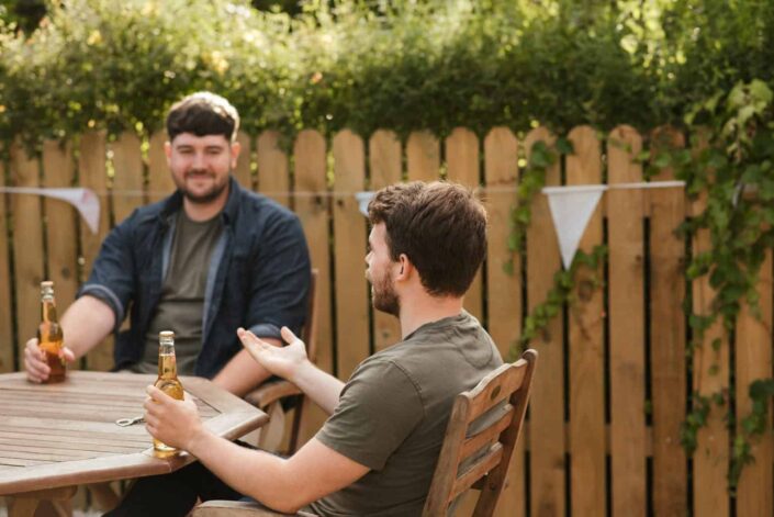 Two guys drinking beer on their garden while having a chat