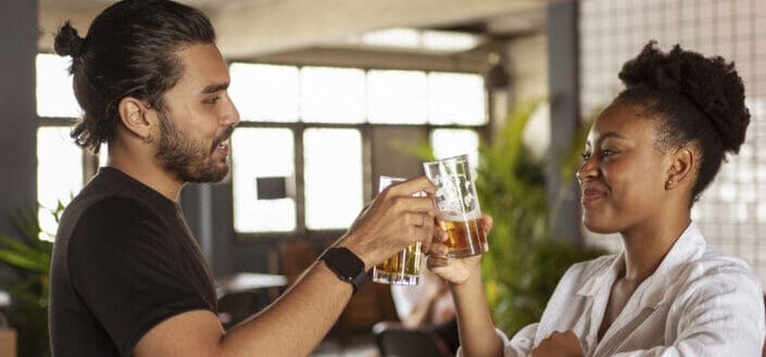 Man and Woman Clinking Two Drinking Glasses Filled With Beer