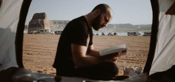 Person reading book outside his tent