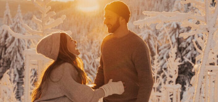 Couple having fun outside a snowy place while the sun is shyly rising