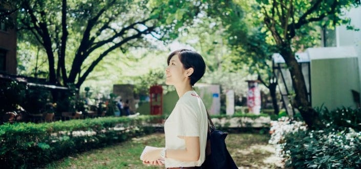 A short haired woman enjoying the sunlight while under the green trees