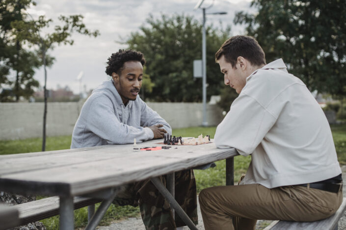 Serious youthful diverse friends playing chess in park