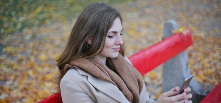 Woman in Coat Holding Smartphone Sitting on Bench
