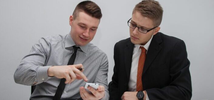 Two men in formal suit looking for an item on the phone.