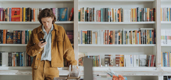 man using phone in front of bookcases